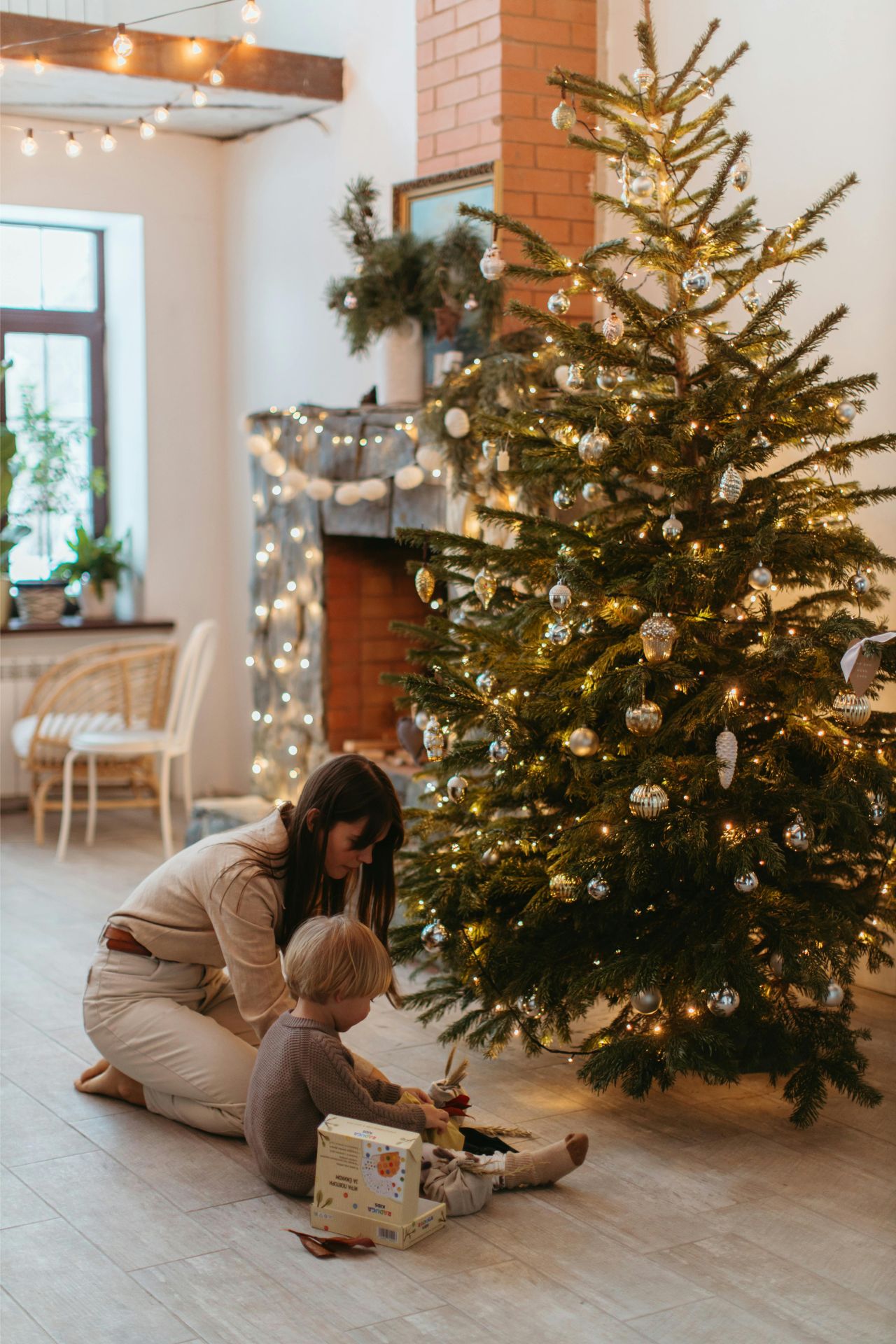 a mother helping a child unwrap a present in front of a christmas tree